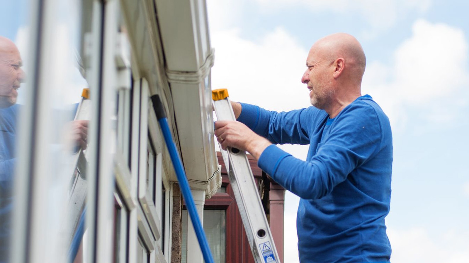 Mand på stige ved hus