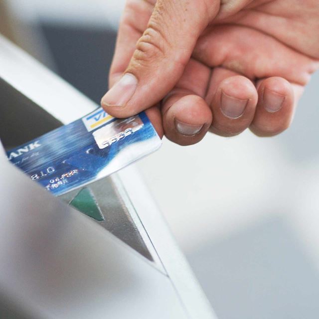 En hånd stikker et betalingskort ind i en pengeautomat
